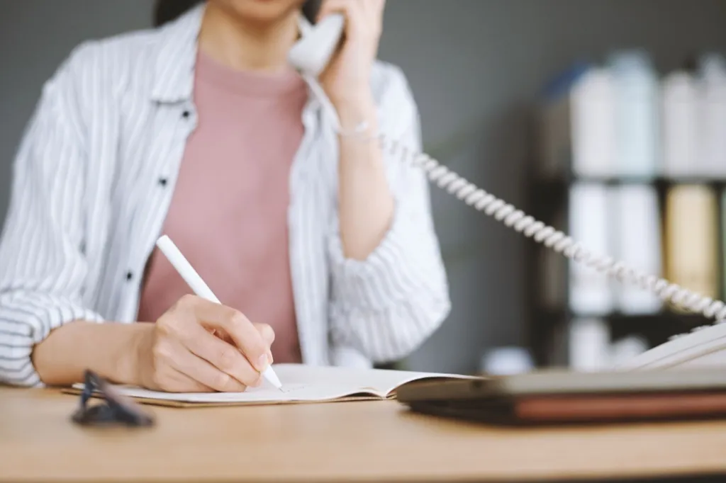 Hands writing notes in a claim diary next to a phone